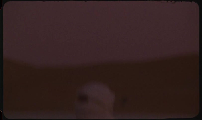 Woman wearing a face and head covering rides on the side of a luxury car in the desert after dusk