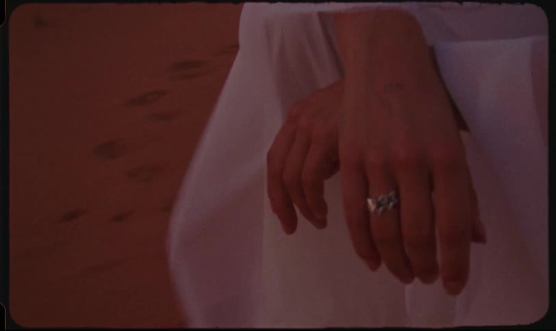 A womans hands with a ring standing on the sand her clothes blowing in the wind