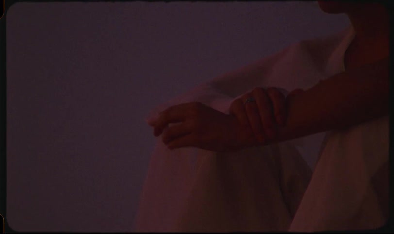 Woman sitting outdoors in a white outfit and moving her fingers