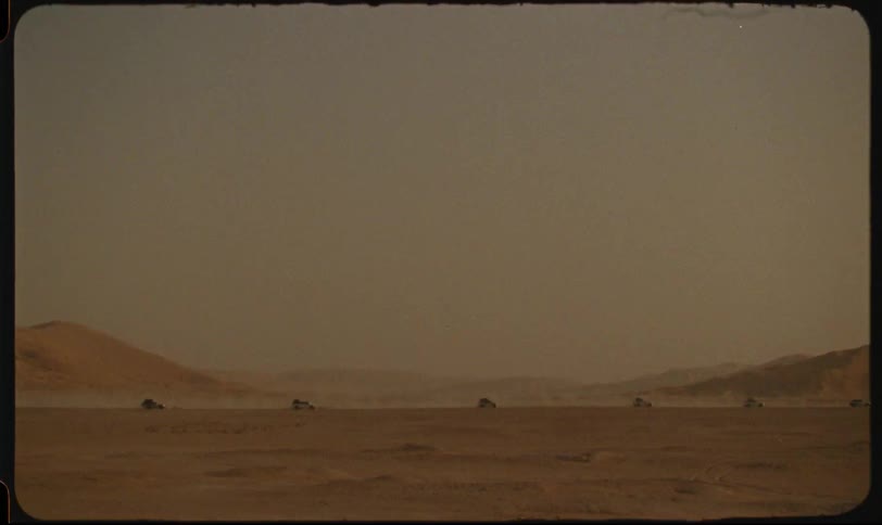 Line of vehicles drives across the desert filling the air with dust