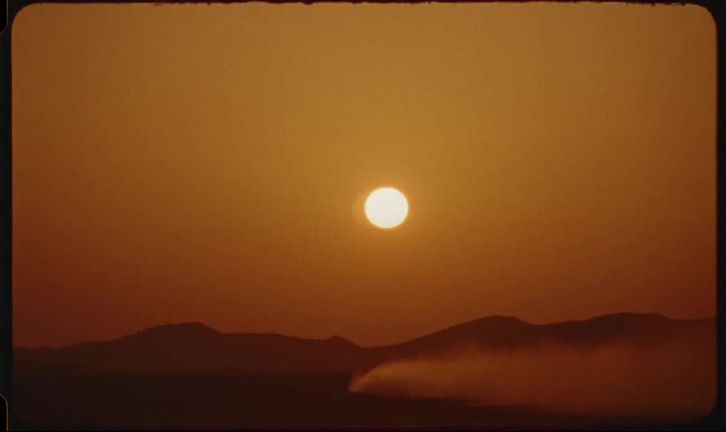 Astronomical object hanging in a red sky shines onto a hazy landscape while smoke rises and flows across the terrain