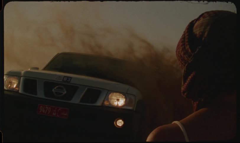 Woman in foreground watching a pickup truck speeding up and sending desert sand flying