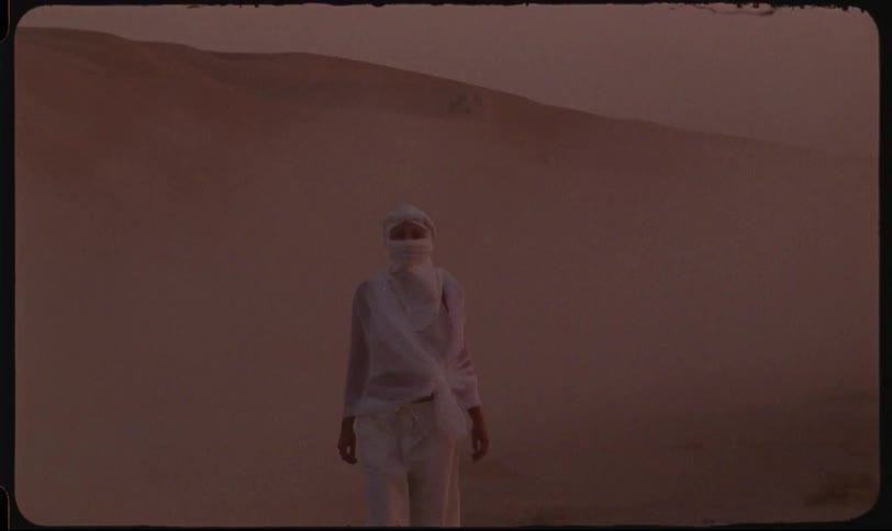 Person in white walking in the desert at sunset and four pickup trucks speeding past