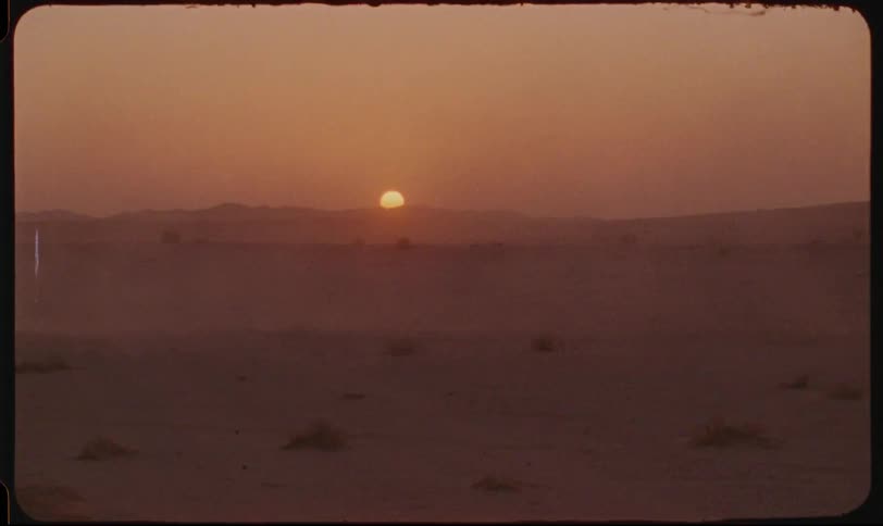 An suv speeds through a dusty desert landscape as the sun sets behind distant hills