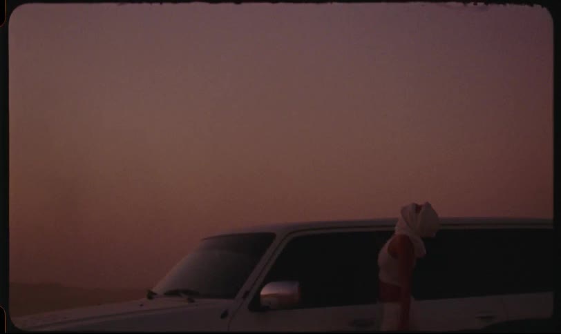 Woman with white scarf over her face leaning on a pickup truck in the desert