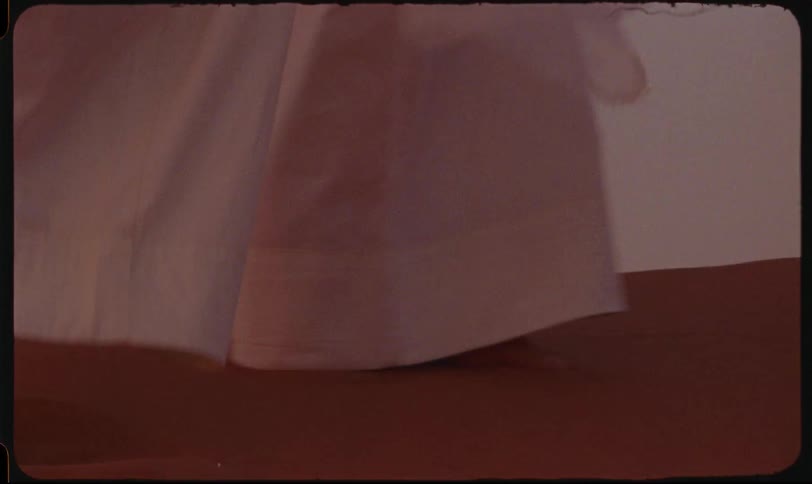 Bare feet and the hem of a white garment are seen walking across a sand dune