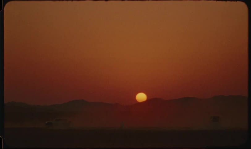 The visible sun setting in the desert as cars drive by the dark desert roadthe sun visibly setting over the desert as cars drive along a dark desert road