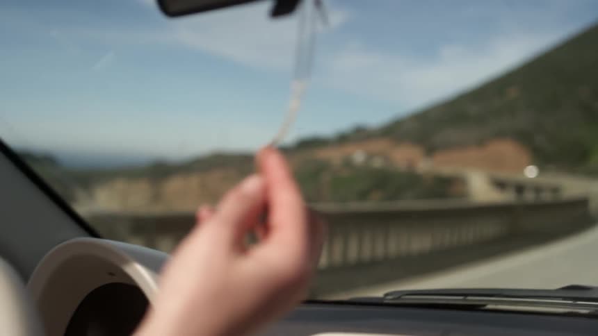 A person touches a necklace hanging from the rearview mirror of a car