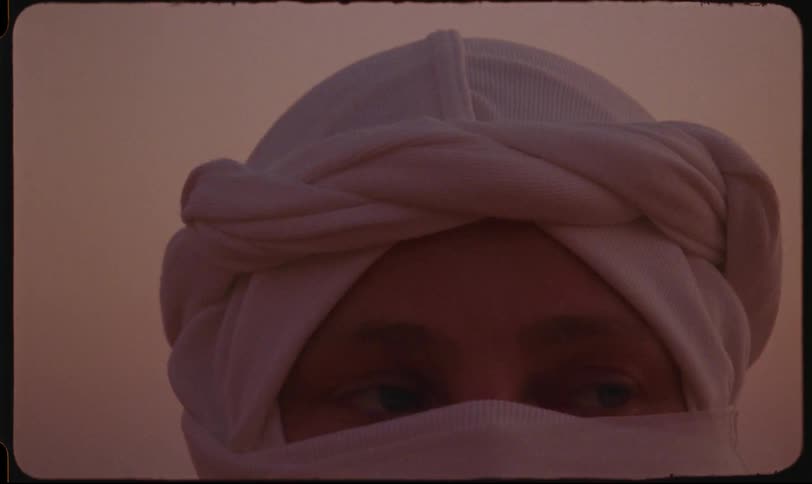 A woman wearing a hijab walking in the desert dragging a piece of wood along the sand