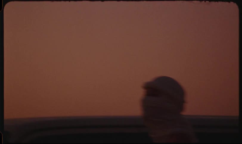 Person with a white scarf covering their head and face next to a vehicle in an outdoor setting in the late afternoon