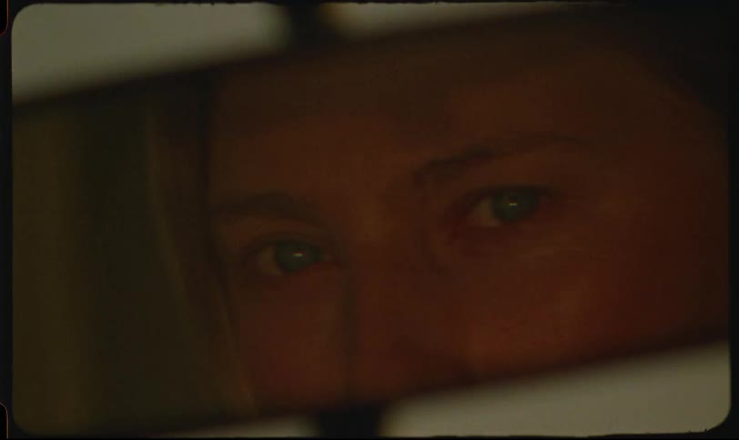 Face of a blonde woman with light eyes seen through a vehicles rearview mirror