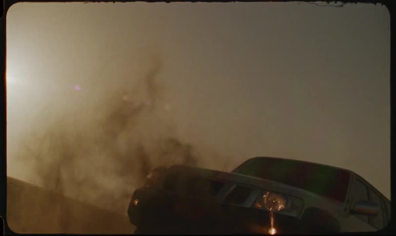 A car aggressively drifts through sand in the desert at sunset kicking up a large dust cloud