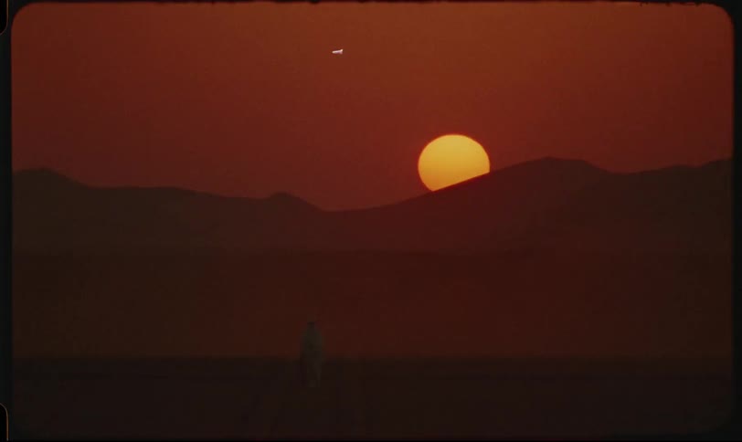 A lone figure walks through a hazy desert landscape at sunset