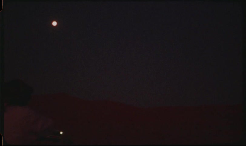 Person in the desert at night making hand signal and a vehicle passing in the background