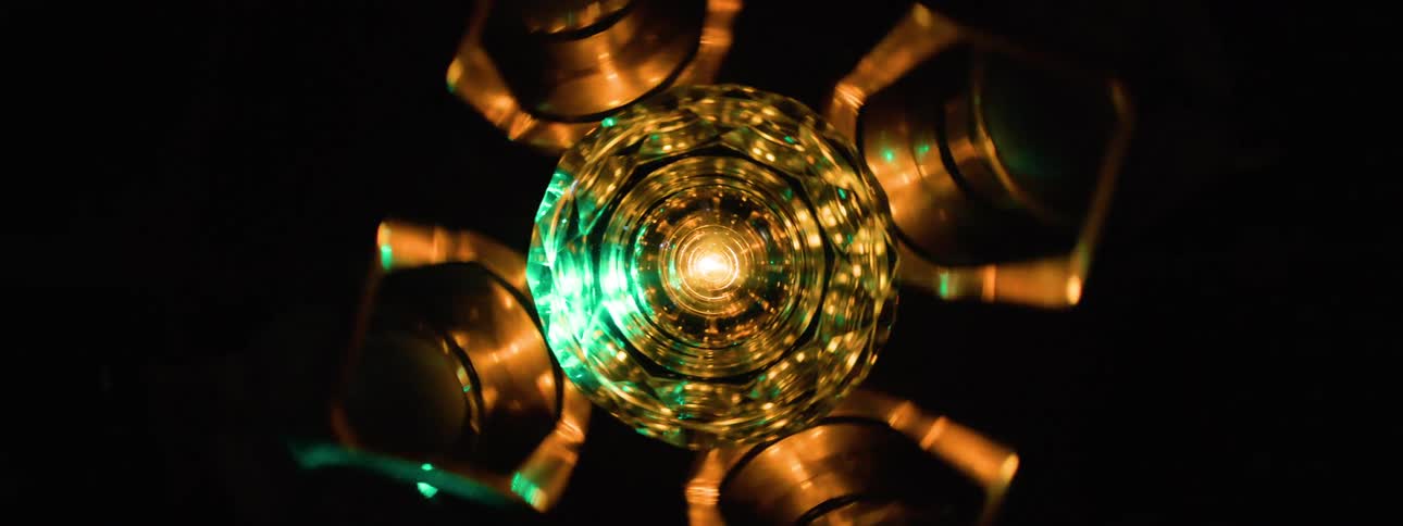 Green light flashes over a center disk surrounded by golden metal cylinders in a rotating machine