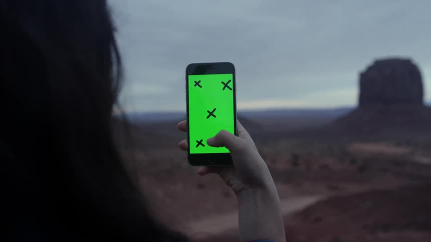 A woman holds her phone up to a desert landscape