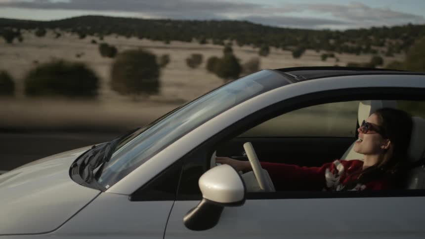 A woman is driving in a car wearing sunglasses