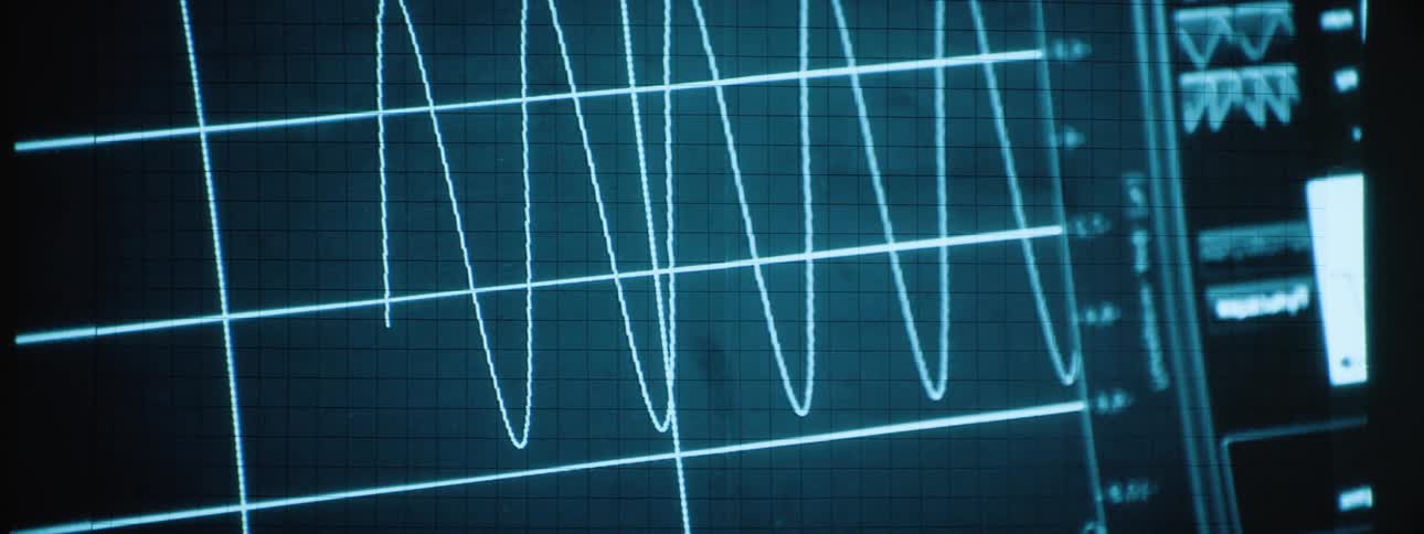A waveform signal is displayed on a digital oscilloscope screen in a bluetinted lab setting