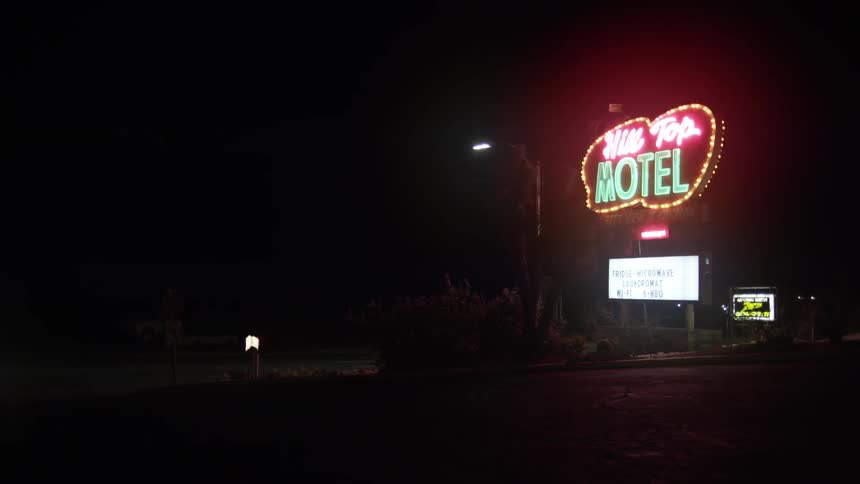 A car pulls into a motel parking lot at night