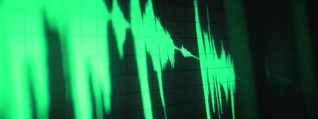 A vibrant green waveform fluctuates across a dark screen with a subtle grid representing an audio signal