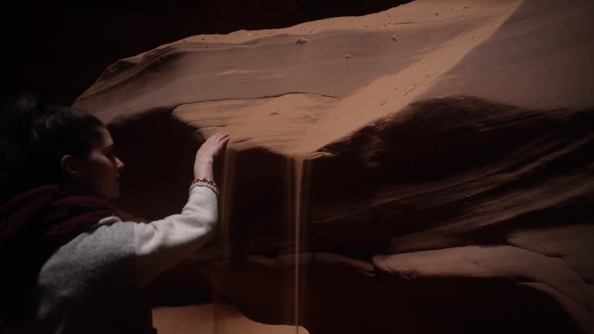 A woman in a cave scooping dirt off of a rock