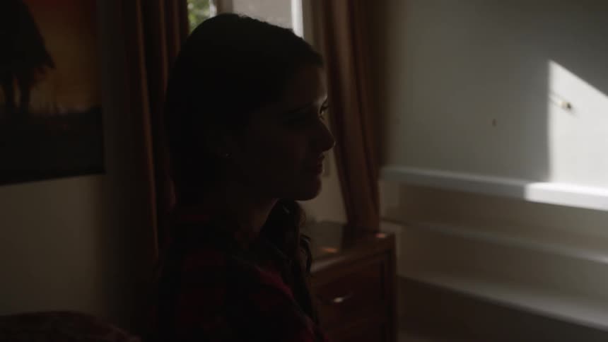 Woman stands in a dark living room looking sad