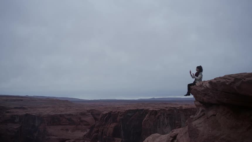 A woman hangs with her feet over a ledge while looking at her phone