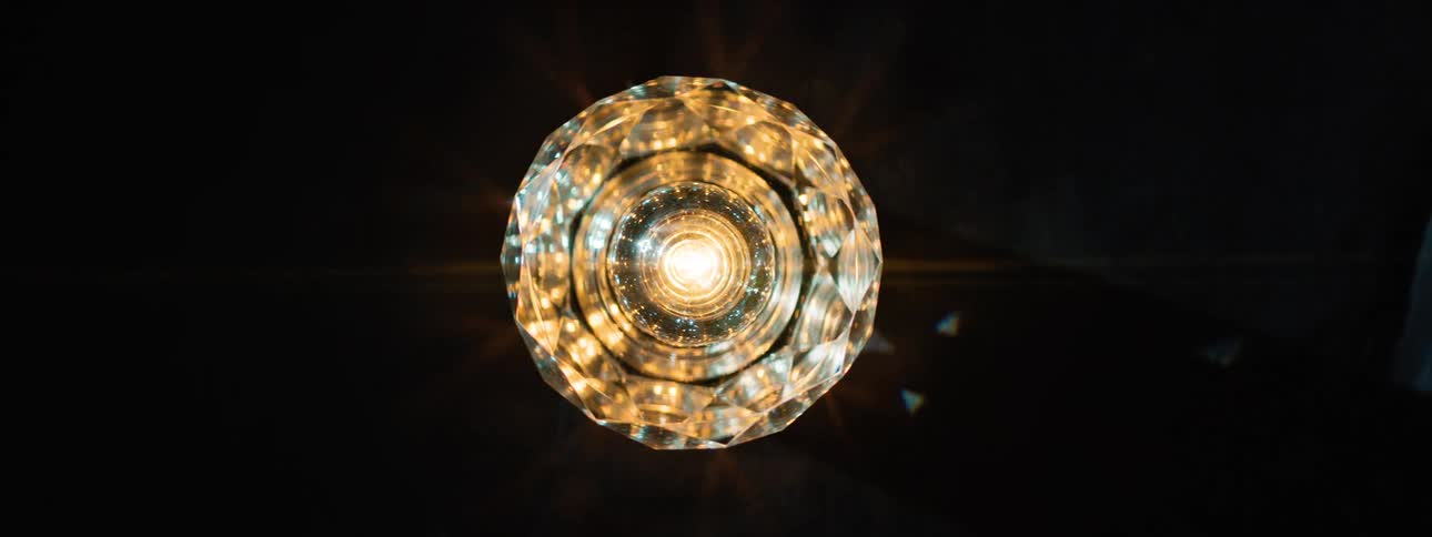 A multifaceted illuminated crystal lamp with internal geometric patterns glows while spinning against a dark background