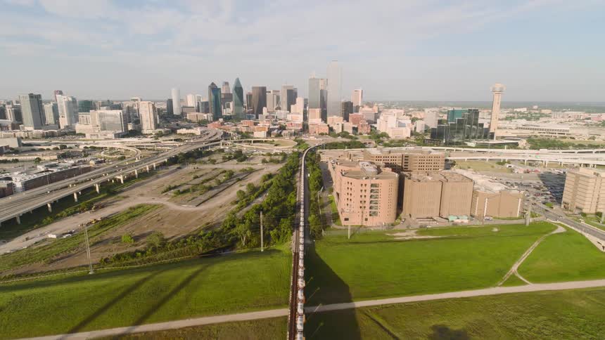 Train crosses a bridge before continuing on tracks paralleling a freeway heading toward the city