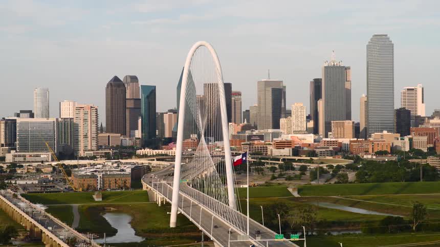 A large bridge with a huge arch and a pole with the chilean flag with tall buildings in the background