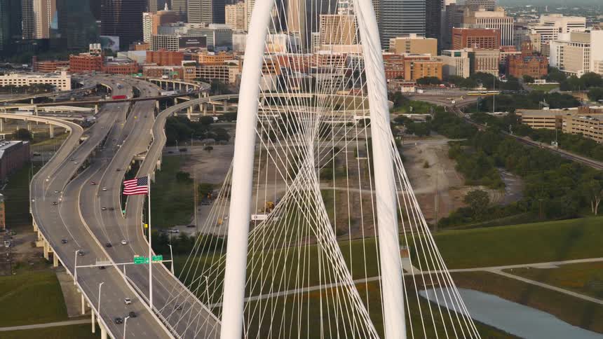 A bridge connecting two cities with an american flag hoisted in front as cars pass by at midday