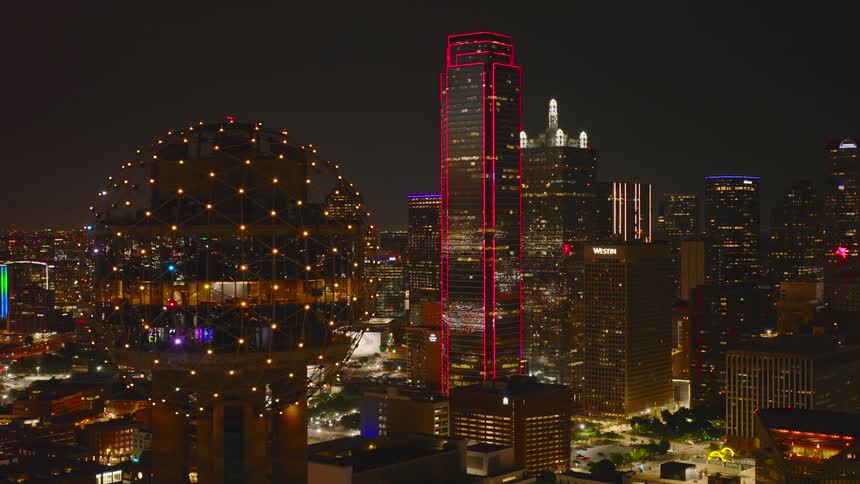 A city skyline view with the reunion tower illuminated by a series of lights at night
