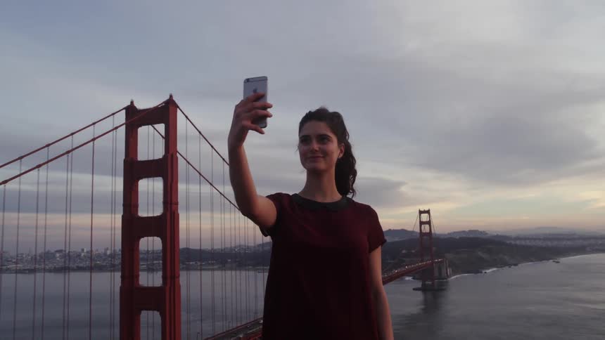 A woman takes a selfie in front of a large bridge
