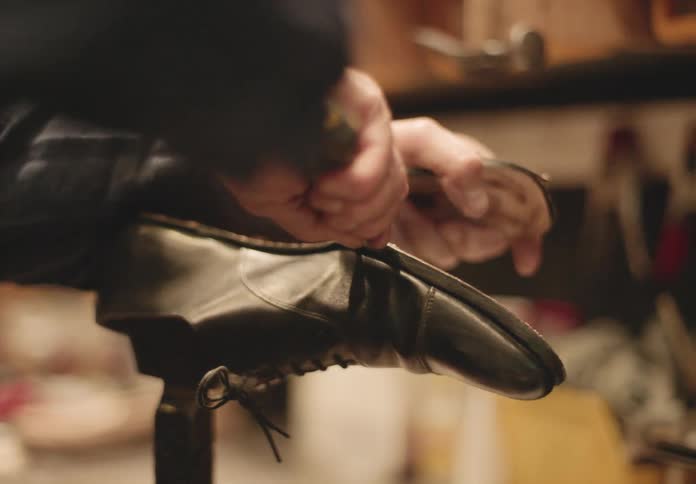 Older cobbler works on a shoe while in his shop