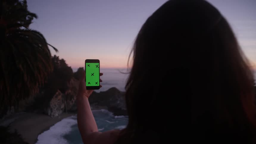 A woman takes a photo of the ocean at sunset