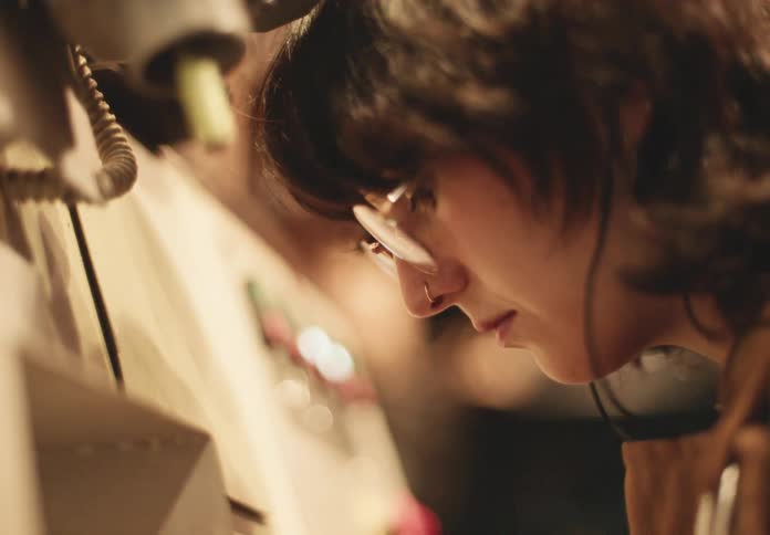 A craftswoman works on a shoe sole against a rotating abrasive belt in a workshop