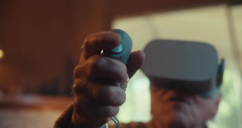 An elderly man with virtual reality headset on and and controller indoor at midday