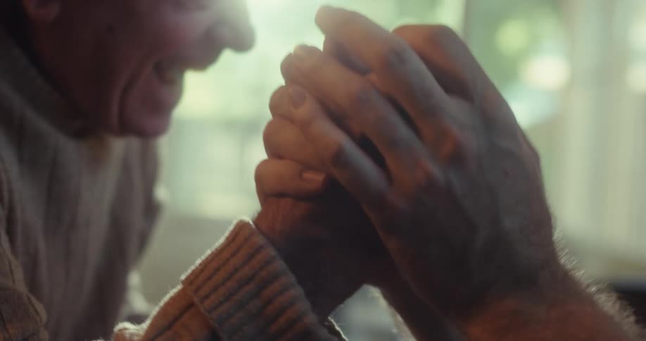 An elderly person and a younger adult clasp hands warmly in a tender emotional moment