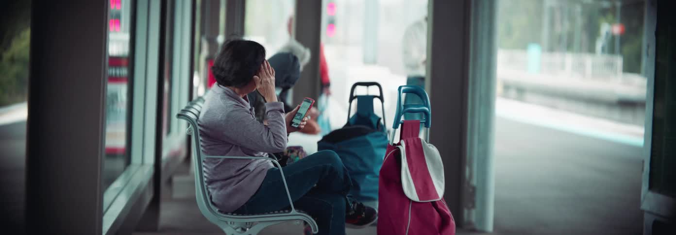 An elderly woman sitting at a train station terminal using her cellphone