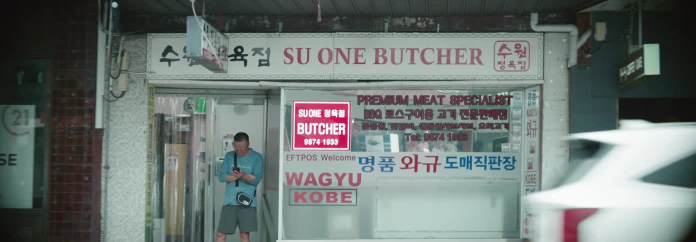 Man looks at his phone while standing in front of a butcher shop