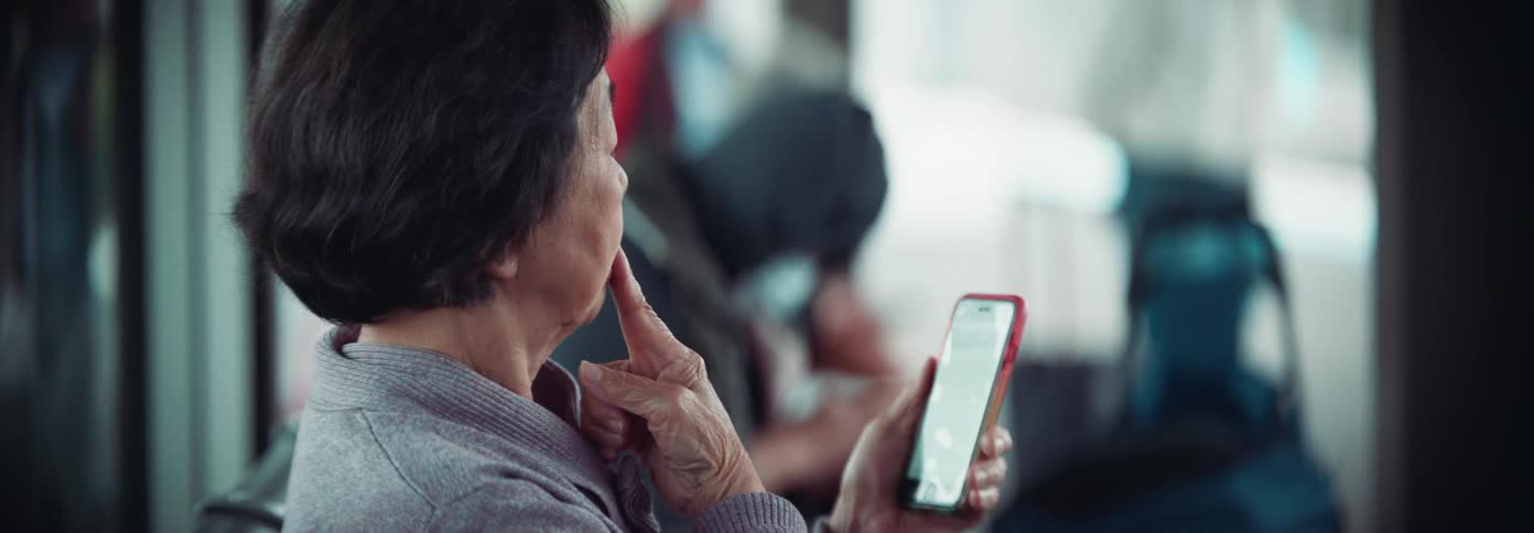 Elderly woman sits in a public place focused on her smartphone screen
