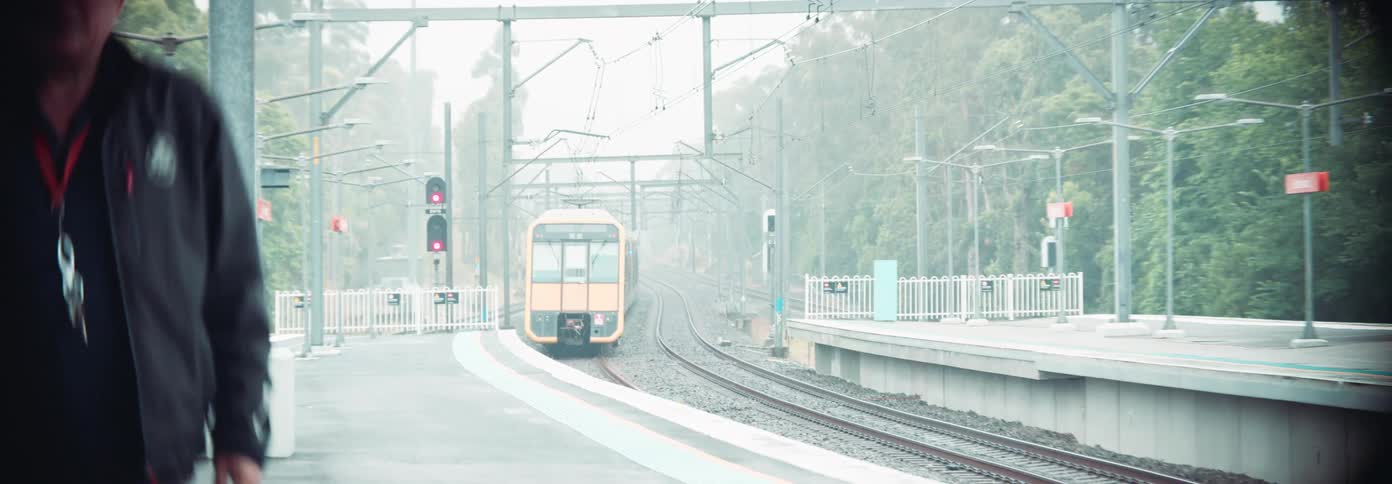 A train approaches a station as two people walk along the platform on a misty day