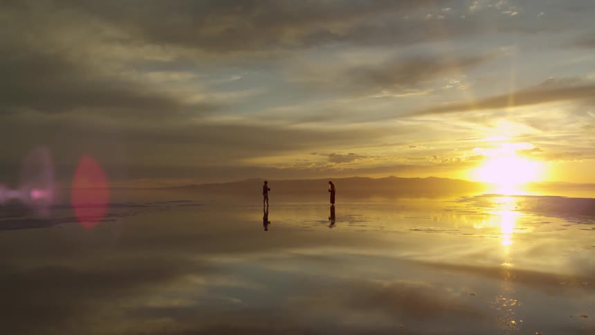 Two silhouetted people stand on a beach at sunset