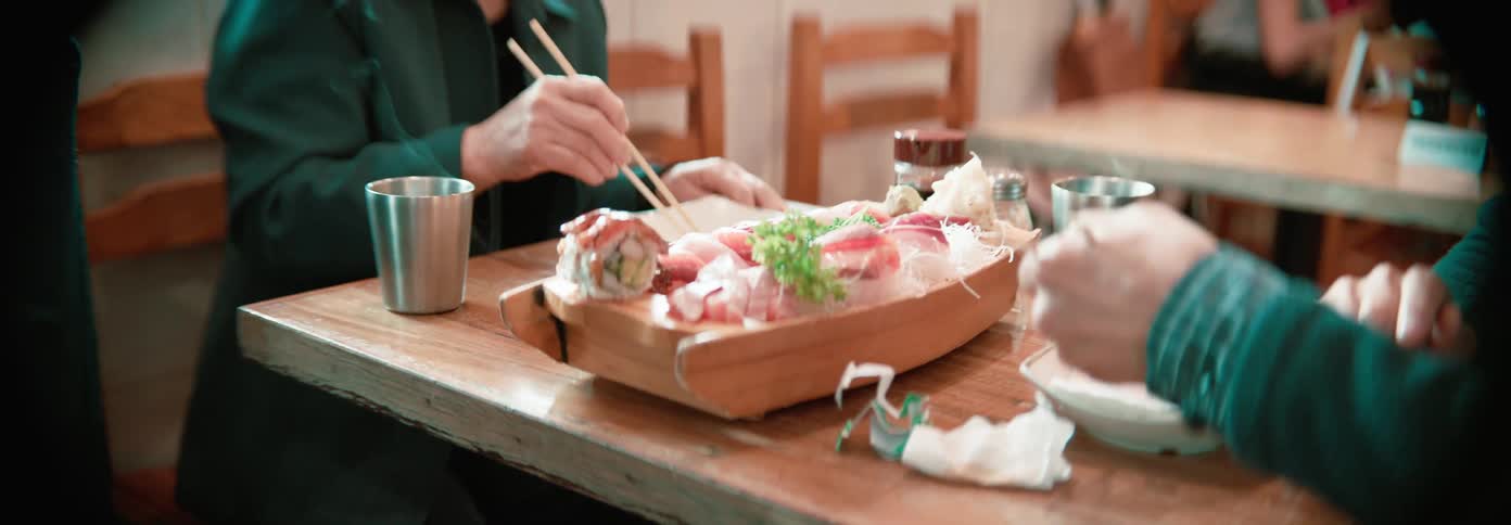Two people in a restaurant eating sushi with chopsticks