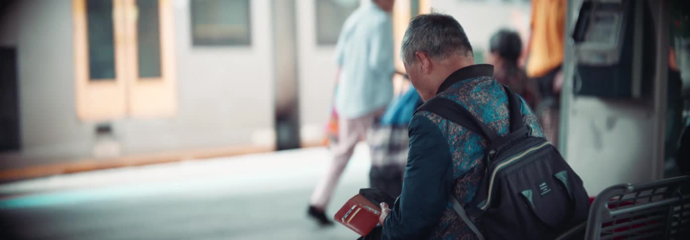 A man is sitting while other men walk around a train station as a train arrives