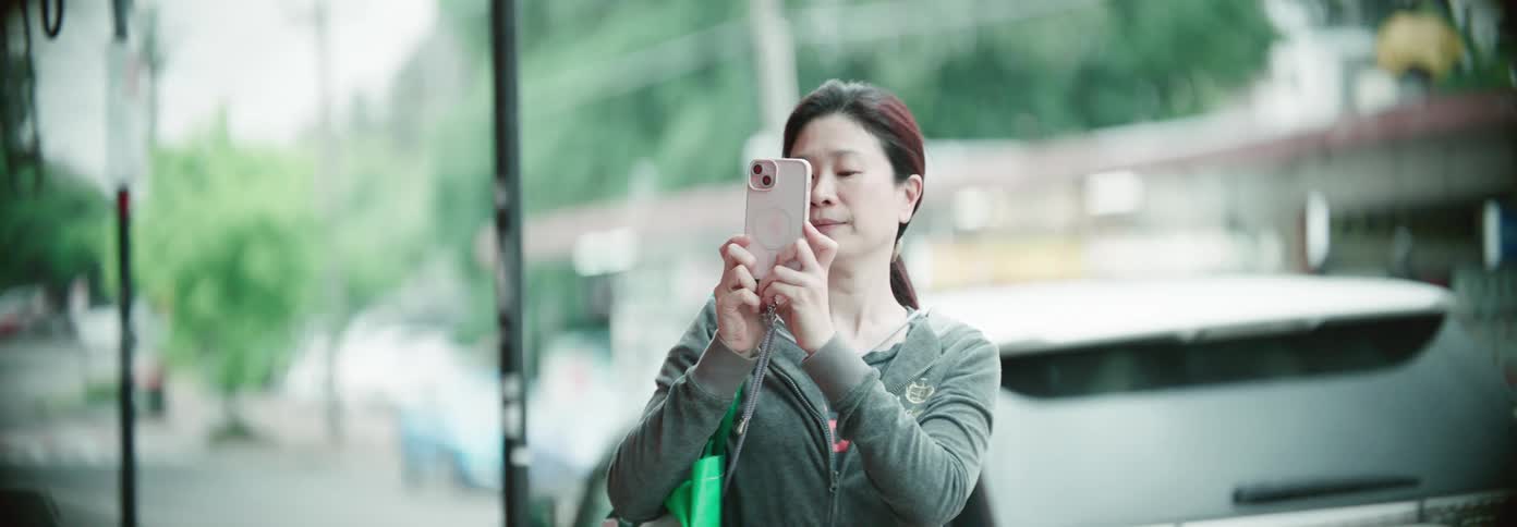 Asian woman records with her iphone in front of a street during the day