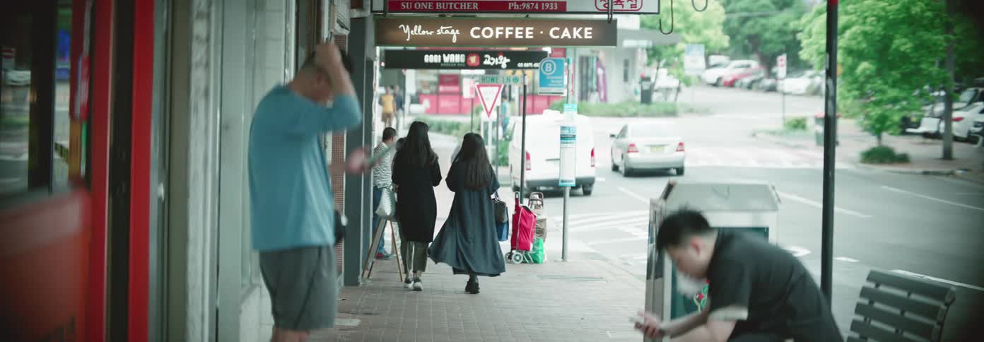 Pedestrians walk past a cafe while other people waiting near a building look at their smartphones