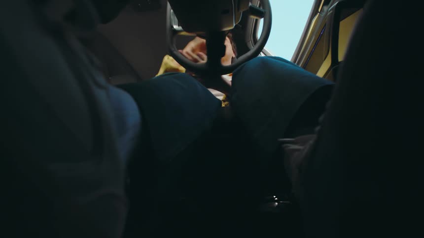 POV in a car from the driver's side floorboard accelerator and brake pedals of a woman driving with her hands on the steering wheel as she turns the vehicle.