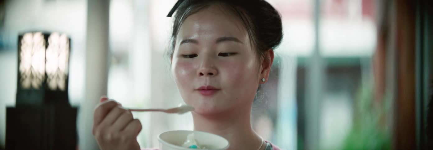 A young woman looks directly at the camera while eating a spoonful of ice cream