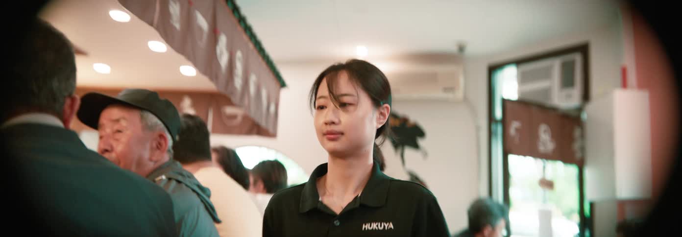 A waitress walks through a busy asian restaurant serving seated customers